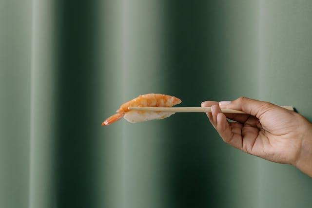 Woman Holding a Piece of Sushi between Chopsticks